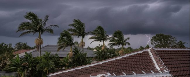 Modern Brisbane home with a solid, freshly repointed tiled roof standing strong against approaching dark storm clouds, symbolizing storm season readiness.