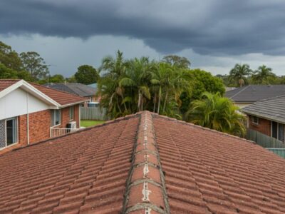 Brisbane home with a tiled roof and ridge capping showing minor cracks in repointing under summer storm clouds.