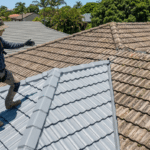 A roofer inspects a roof split between new grey tile coating and old weathered terracotta.